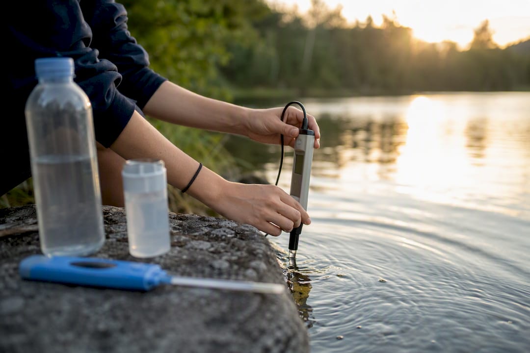 Hands calibrating pH meter at stream bank