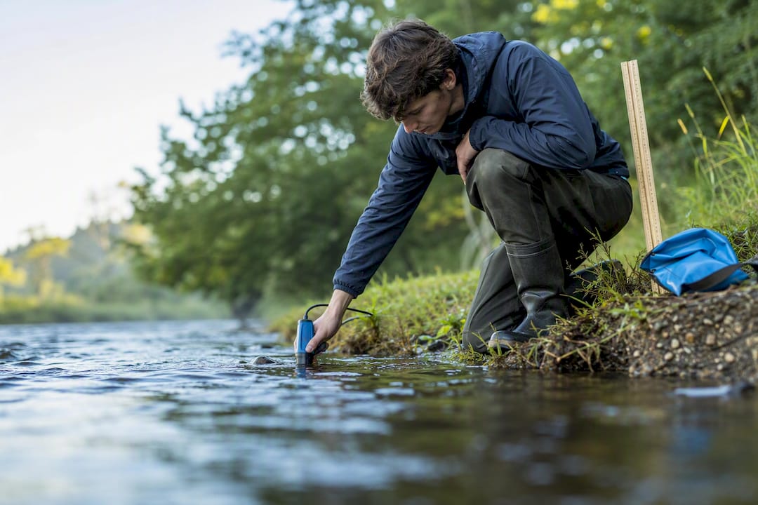 Student measuring river velocity with flow meter